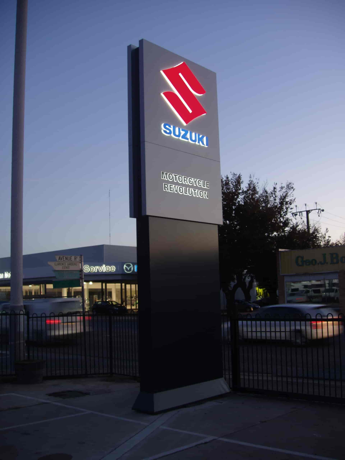 Illuminated pylon sign with halo-lit logo panels and tenant message at dusk