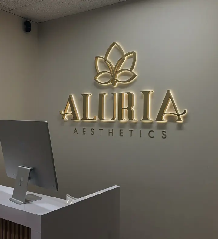 Aluria Aesthetics halo-lit gold letters and lotus emblem glowing warm white on a medspa reception wall