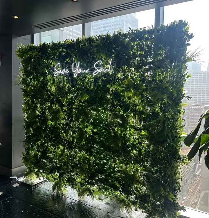 White script LED neon sign reading Save Your Soul on a greenery wall at ROOF on theWit, Chicago
